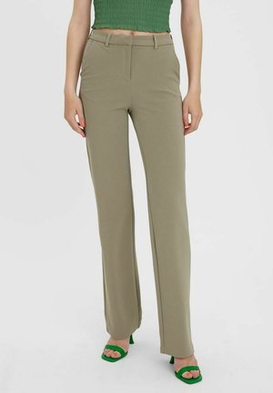 Woman wearing high-waist beige straight-leg pants, green ruched crop top, and green open-toe heeled sandals, standing against a white background.