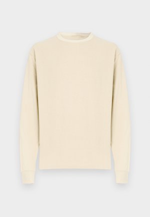 Majica z dolgimi rokavi in okroglim izrezom v svetlo bež barvi, izdelana iz mehke bombažne tkanine. Ima rebraste manšete in raven spodnji rob, brez vidnih vzorcev ali grafičnih motivov.