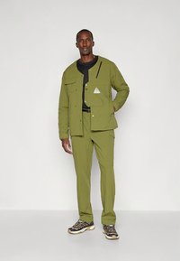 Zielony zestaw bluzy i spodni wykonany z lekkiego materiału. Bluza posiada dwie przednie kieszenie, trójkątną naszywkę oraz czarny zamek błyskawiczny jako akcent.