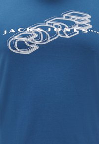 Modrá bavlněná trička s bílým grafickým textem, který zní "JACK & JONES" a "CORE" s obrysovými blokovými písmeny.