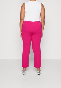 Figurerade, ankellånga byxor i ett klart rosa tyg med en slät yta. Bakvy visar ett sömlöst midjeband och minimal detaljering.