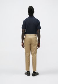 Σκούρο μπλε πολο πουκάμισο με κοντά μανίκια, συνδυασμένο με ανοιχτό μπεζ παντελόνι με στενή γραμμή. Λείο ύφασμα, επίπεδες τσέπες και καφέ παπούτσια.