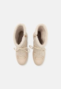 Bottes d'hiver beige avec un intérieur doux et moelleux, dotées d'un extérieur lisse et de lacets légers. Accents en matériel doré près de la cheville.