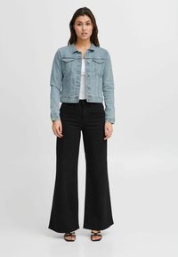 Chaqueta de mezclilla azul claro con un diseño clásico, combinada con pantalones de pierna ancha negros de cintura alta y sandalias negras con tiras.