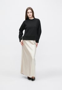 Μαύρο φούτερ με ακάλυπτους ώμους συνδυασμένο με σατέν μπεζ μακριά φούστα. Το μοντέλο φοράει μαύρα παπούτσια με μυτερή μύτη. Απλή και κομψή ενδυμασία.