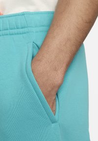 Pantalones de chándal turquesas con cintura elástica, que cuentan con bolsillos laterales y una textura suave, con costura detallada en la cintura.