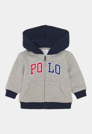 Jasnoszara bluza z kapturem z przednim zamkiem błyskawicznym, granatowymi detalami i napisem "PO LO" w czerwonych i niebieskich literach. Posiada boczne kieszenie i ściągacze na rękawach.