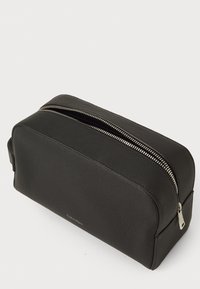 Black textured leather toiletry bag with silver zipper partially open, rectangular shape, and Calvin Klein logo on side.