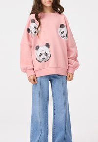 Pink sweatshirt made of cotton with loose fit, featuring four panda head appliqués in black and white. Paired with wide-leg denim jeans.