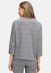 Veste à carreaux grise, coupe ample, manches trois-quarts et col montant. Tissu texturé avec de subtils accents bruns dans le motif.