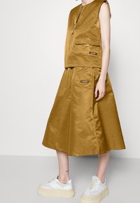 Bronze satin vest with front zipper and pockets, paired with a matching knee-length skirt. White platform sneakers complete the outfit.