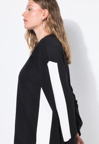 Sudadera negra con rayas diagonales blancas en las mangas. Hecha de una tela suave, con un corte relajado y cuello redondo.
