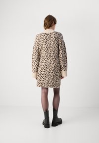 Cardigã de malha com padrão de leopardo em bege e castanho, com gola e punhos canelados. O modelo usa botas pretas até ao tornozelo e meias finas.