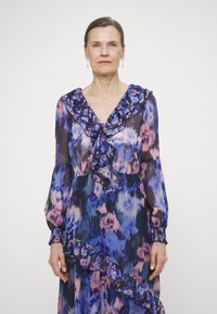 Bloemenpatroon jurk in tinten blauw en roze, met een rimpelachtige halslijn en mouwen, en een tiered rimpelaccent aan de zijkant.