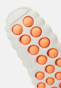 Φωτεινή γκρι σόλα παπουτσιού με κυκλικά πορτοκαλί στοιχεία απορρόφησης κραδασμών, υφή στην επιφάνεια και γλυπτή, κυματιστή σχεδίαση με λογότυπο Nike.