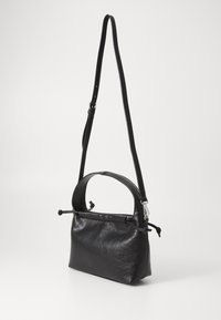 Black leather bag with a structured shape, short handle, and adjustable strap. Surface features a smooth, slightly textured finish.