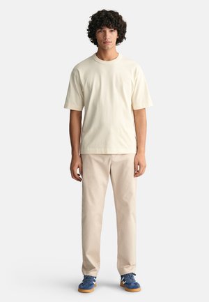 Cream cotton t-shirt, relaxed fit, short sleeves. Beige pants, straight cut. Blue sneakers with white accents and gum sole, worn casually.