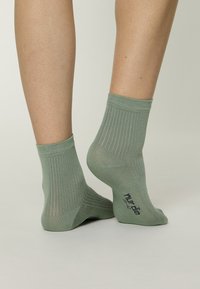 Calcetines verdes acanalados con un puño de longitud media. Hechos de un material suave y texturizado. Presentan un logo impreso en el lado exterior.