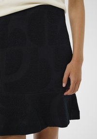 Jupe texturée noire avec un design en côtes et des motifs abstraits, un ourlet évasé et une taille lisse.