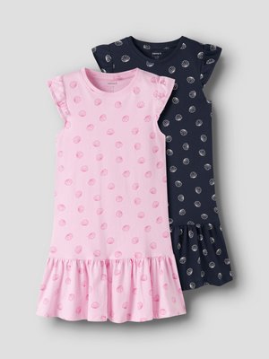 Dve brezrokavni dekliški obleki z volančki na robovih, ena roza z roza potiski morskih školjk in ena temno modra z belimi potiski morskih školjk, obe položeni na ravno površino.