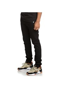 Black skinny jeans paired with black, grey, and orange athletic sneakers featuring a speckled white sole and textured accents.
