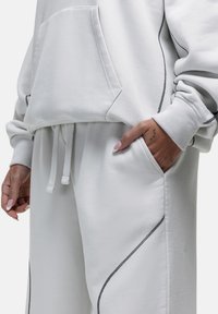 Lichtgrijze hoodie met een voorzak en geribbelde manchetten, gecombineerd met bijpassende trainingbroeken met zwarte accentstiksels en zijzakken.