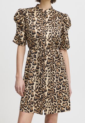 Vrouw die een kort mouw, knoopjurk draagt met luipaardprint en opgeblazen schouders, gestrikt in de taille met een dunne riem.