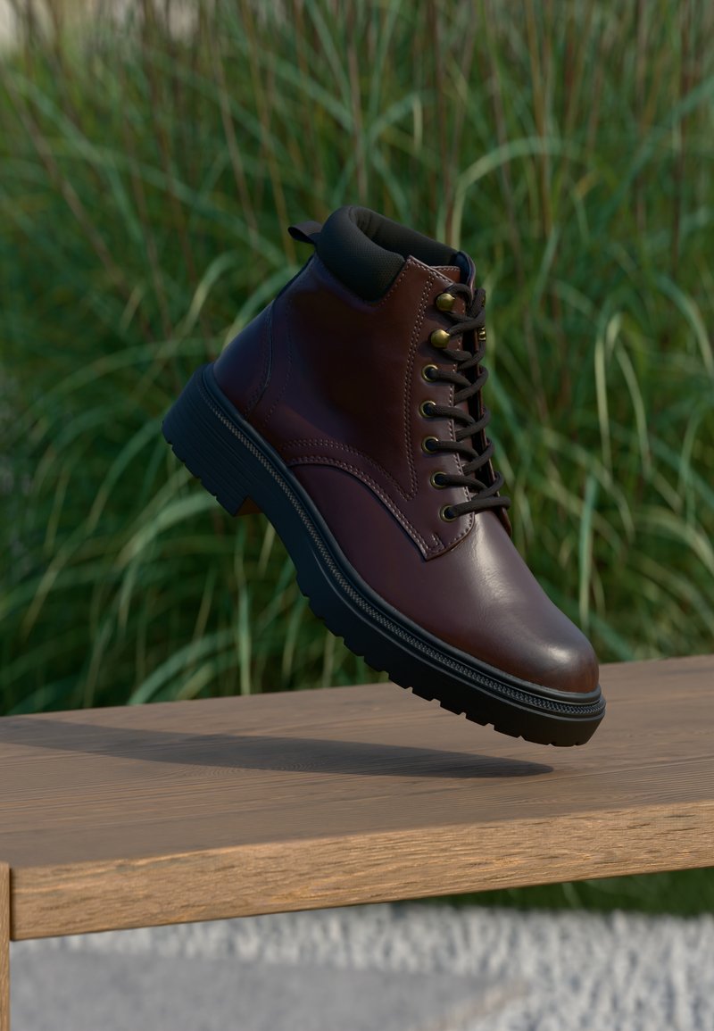 Stivaletto in pelle marrone con accenti neri, punta rotonda e design con lacci. La suola in gomma presenta un battistrada testurizzato per una migliore aderenza.