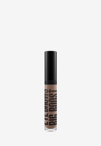 Correcteur liquide dans un tube en verre transparent avec un capuchon noir. Le tube présente un motif géométrique noir sur un fond beige.