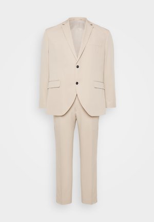 Costume beige en deux pièces fabriqué en tissu lisse. Comprend un revers cranté, une veste à boutonnière simple avec des boutons noirs, et un pantalon droit.