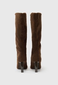 Cizme maro, pufoase, până la genunchi, cu o textură finisată, având un toc bloc elegant. Designul este ajustat, cu partea superioară rotunjită.