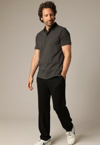 Polo noir à manches courtes avec un motif à pois et un col contrasté, associé à un pantalon noir et des baskets blanches avec des accents bleus.