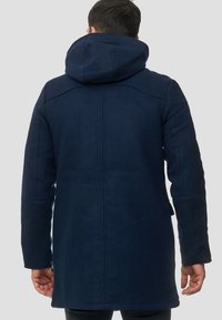 Abrigo de mezcla de lana azul marino con capucha, corte recto, ventanales en la parte trasera y bolsillos laterales. Presenta detalles de costura y una textura suave.