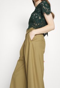Groene kanten crop top met korte mouwen; gecombineerd met hoge taille, wijdvallende kaki broeken met zijzakken en een soepele textuur.