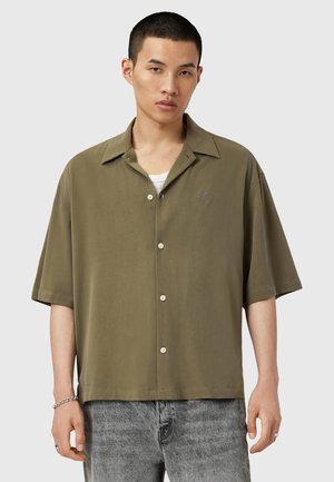 Chemise à manches courtes olive en coton, fabriquée dans un tissu lisse. Dotée d'un logo en forme de cœur subtil sur la poitrine et de boutons clairs.