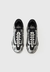 Buty New Balance w kolorze czarnym i srebrnym. Wykonane z mieszanki siateczki i materiałów syntetycznych, z teksturowaną podeszwą i widocznym logo po bokach.