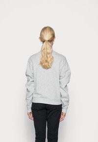 Lichtgrijze pullover sweatshirt met een relaxte fit, ribgebreide manchetten en zoom, en doorgeschoven schouders. Gekleed met donkere broek, gezien vanaf de achterkant.