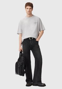 T-shirt gris surdimensionné avec des manches courtes et un logo ; jean noir à jambes larges ; sac à dos noir texturé ; chaussures noires épaisses ; coupe décontractée.