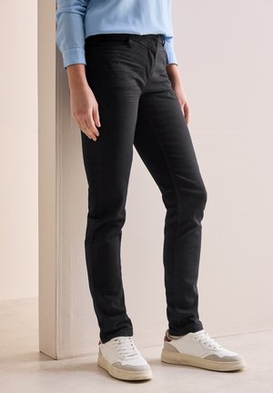 Jeans en denim noir avec une coupe slim, dotés de poches avant et d'une texture lisse, accompagnés de baskets blanches et d'un haut bleu clair.