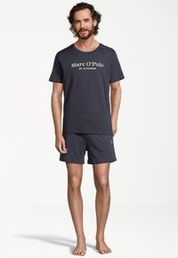 Maglietta da uomo in cotone grigio scuro con logo bianco "Marc O'Polo" sul petto, abbinata a pantaloni corti coordinati dal design semplice.