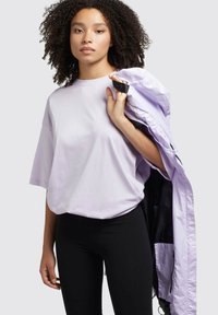 Tricou oversized lavandă cu mâneci scurte, asortat cu colanți negri; ținând o jachetă ușoară lavandă cu interior negru.