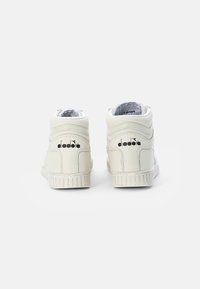 Para off-white wysokich trampek z czarnymi logo Diadora z tyłu, wyeksponowane na białym tle.