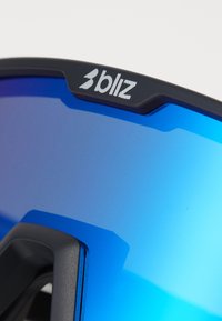 Blautönte Sonnenbrille mit einem schwarzen Kunststoffrahmen, der ein glänzendes Logo und ein gewölbtes Linsendesign aufweist. Die Oberfläche ist glatt und besitzt keine sichtbaren Muster.