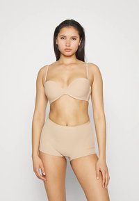 Beiger wattierter BH mit verstellbaren Trägern, kombiniert mit beigen High-Waist-Shorts. Glatte Textur und nahtloses Design.