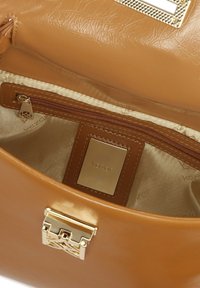 Notranjost usnjene torbice v barvi tan z žepom na zadrgo, zlato obrobo in gladko podlogo s tiskom logotipa.