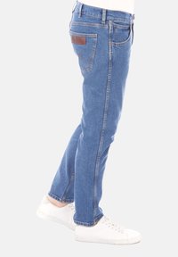 Světlé modré džíny z denimu se střihy rovnýma nohavicemi. Mezi detaily patří hnědá kožená nášivka na zadním pásku a minimální šití.