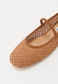 Ballerine beige intrecciate con punta rotonda, dotate di una fascia elastica marrone, lati aperti e una fodera interna liscia. La parte superiore testurizzata aggiunge dettaglio.