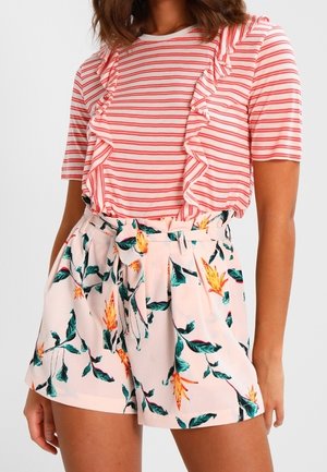 Femme portant un haut rayé rouge et blanc avec des volants et un short taille haute rose avec un imprimé floral vert et jaune.
