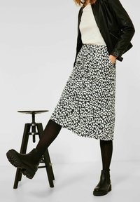 Mekko, jossa on mustavalkoinen kuviointi, midimittainen, laskostettu muotoilu ja taskut, yhdistettynä mustiin nilkkureihin ja nahkatakkiin.