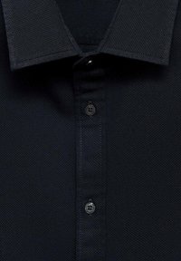 Polo shirt in blu navy con texture, dotato di colletto button-down e un singolo bottone nero sull'apertura con dettagli di cucitura.
